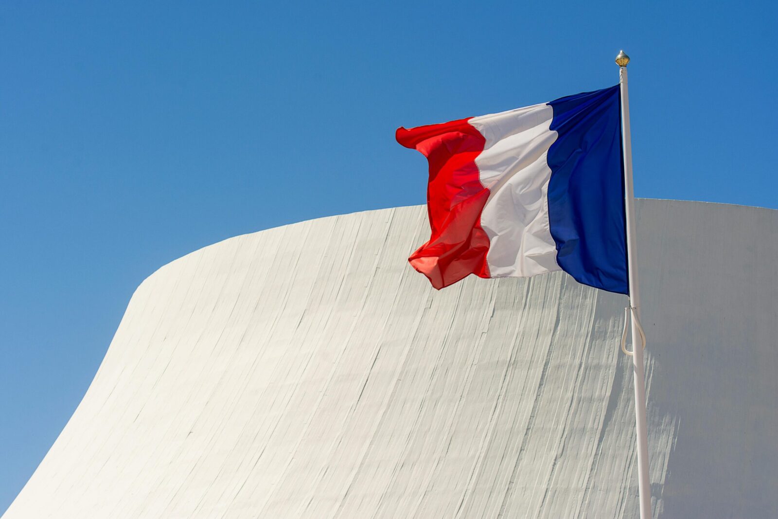 French flag waves against a modern architectural backdrop in Le Havre, Normandië.